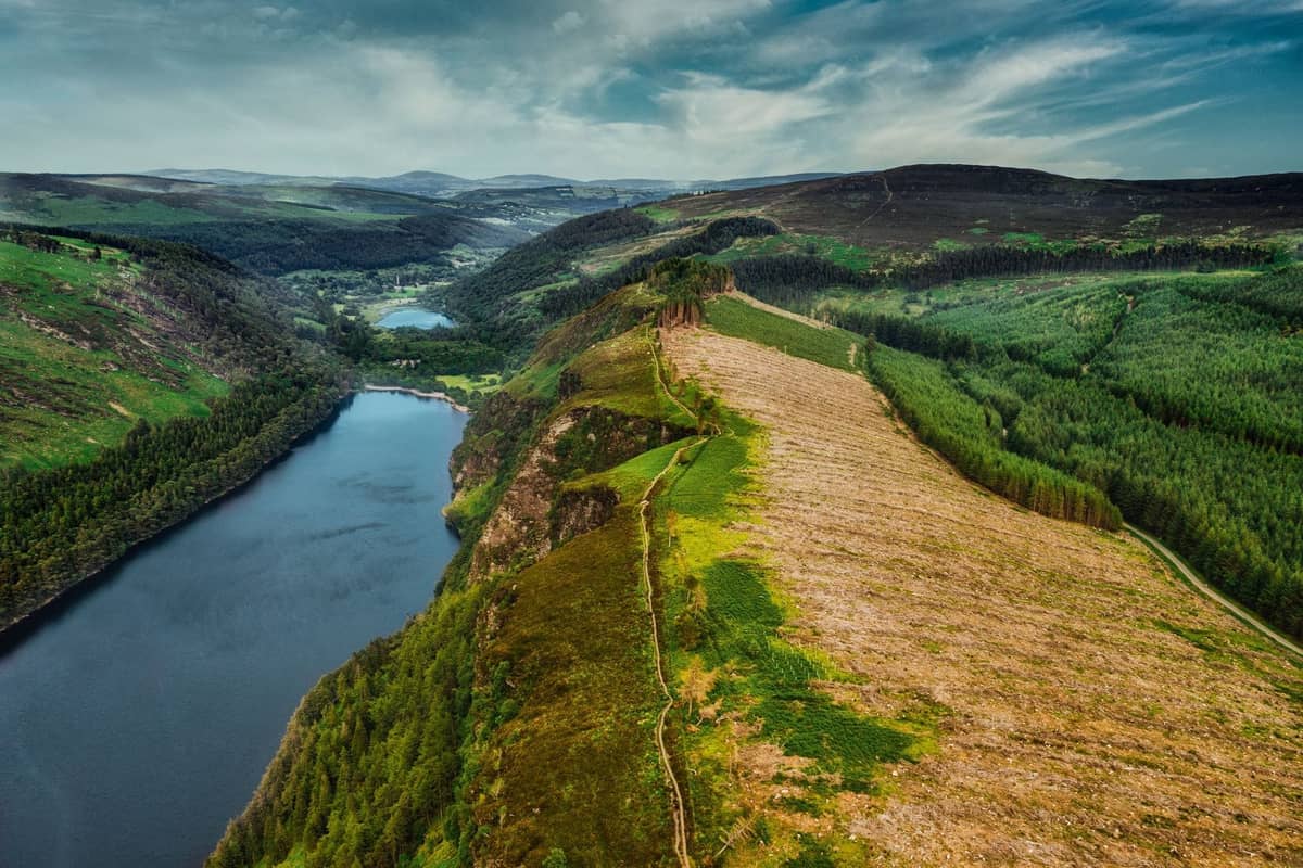 Vue aérienne d'une vallée glaciaire et d'un lac entourés de forêts verdoyantes et de collines dans les montagnes Wicklow par temps clair.