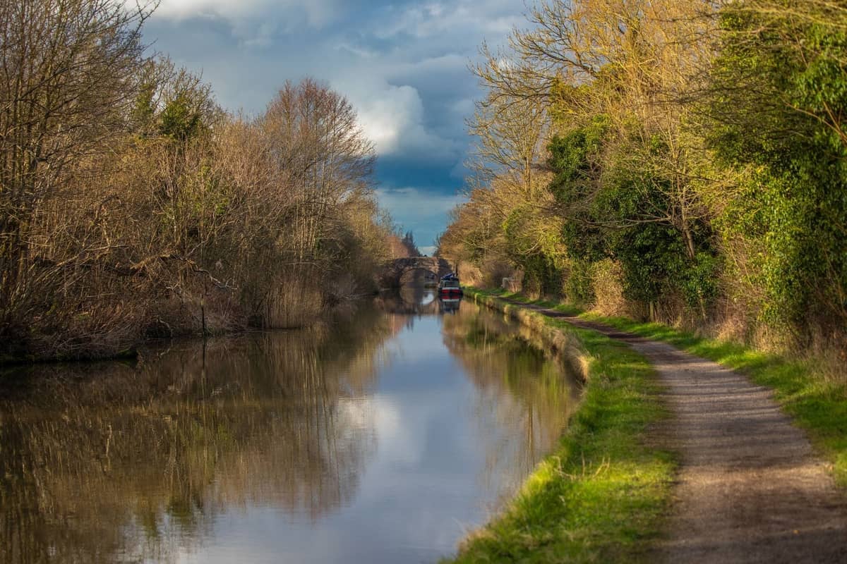 Un chemin de canal paisible bordé de berges herbeuses et d'arbres avec un narrowboat et un pont au loin, idéal pour les promenades dans la nature près de Dublin.