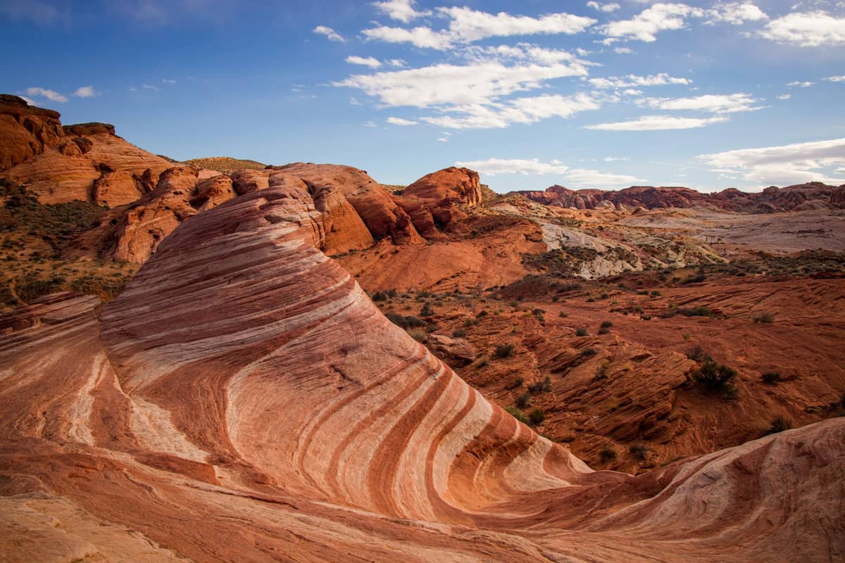 Weitwinkelansicht der Felsformation Fire Wave im Valley of Fire State Park, Nevada, mit wirbelndem rotem und weißem Sandstein unter blauem Himmel.