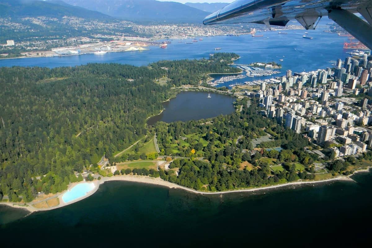 Luftaufnahme des dichten Waldes von Stanley Park, der Lagune, der Stadtsilhouette und der Uferpromenade von Vancouver an einem sonnigen Tag.
