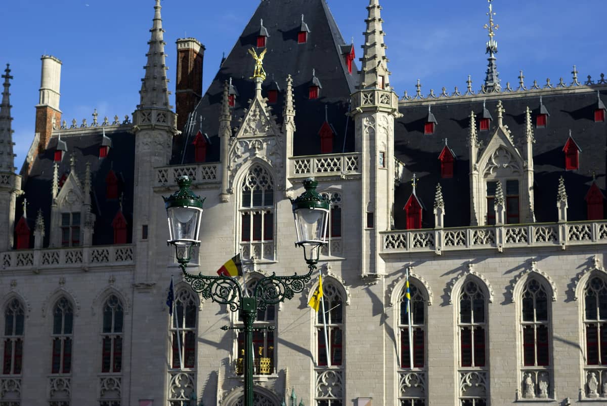 Detailed view of the neo-Gothic Historium Bruges building façade with ornate windows and spires under a clear blue sky.