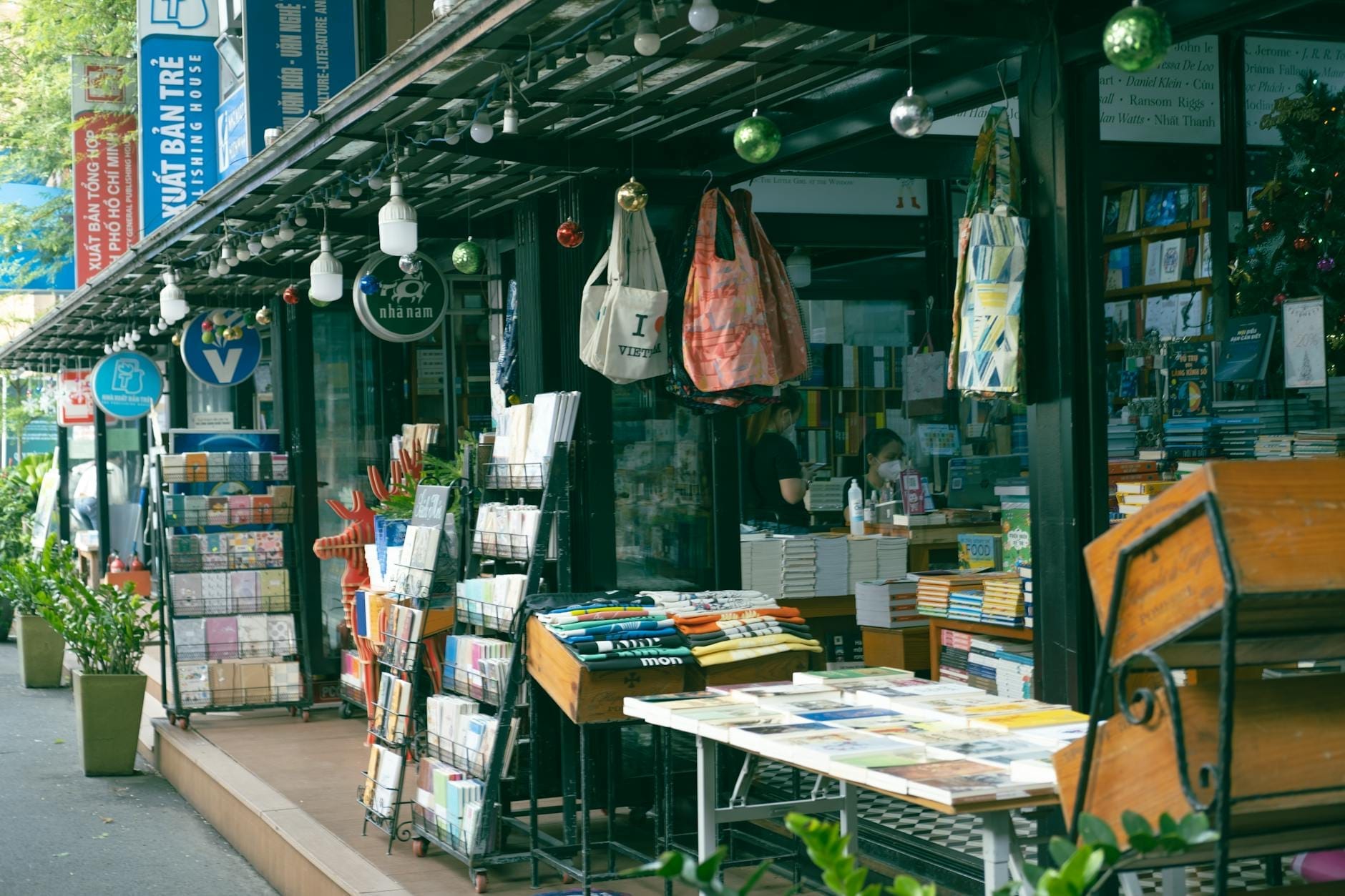 Una encantadora hilera de puestos de libros bajo un toldo, llenos de libros y decorados con plantas colgantes y bolsas de colores en la Calle del Libro de Ciudad Ho Chi Minh.