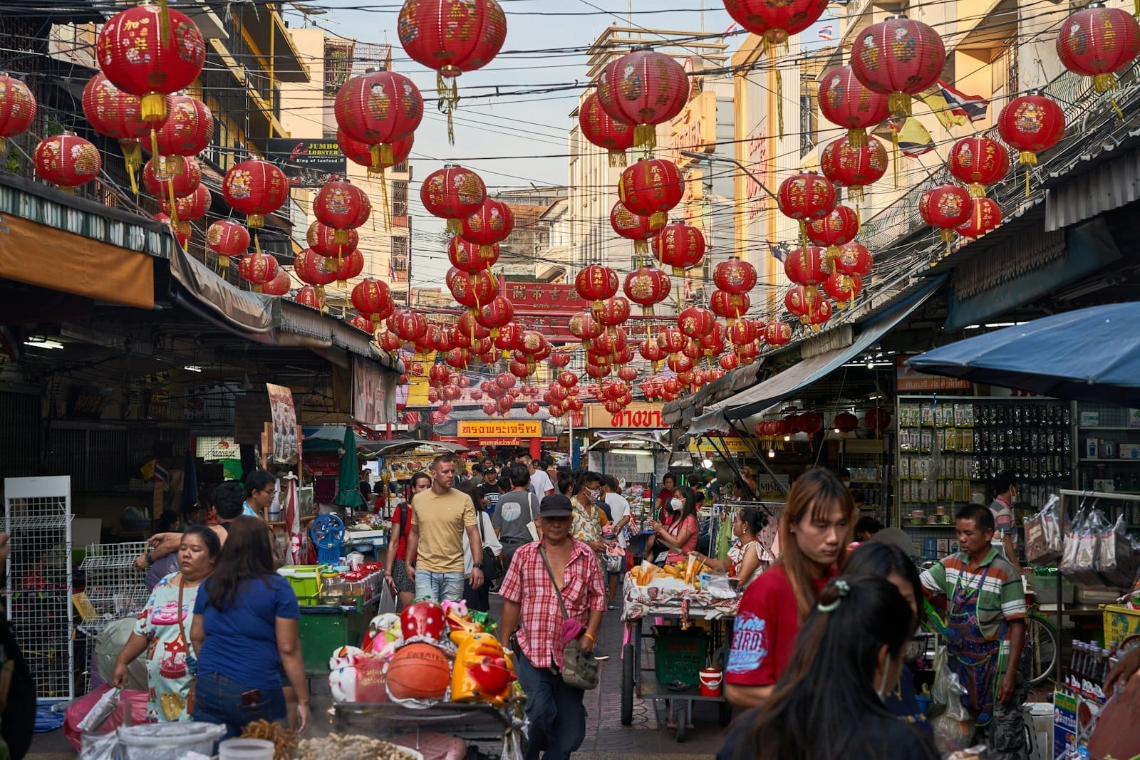 Concurrido mercado callejero en Cholon, Ciudad Ho Chi Minh, con faroles rojos colgantes, compradores ajetreados y puestos de vendedores vibrantes durante el día.