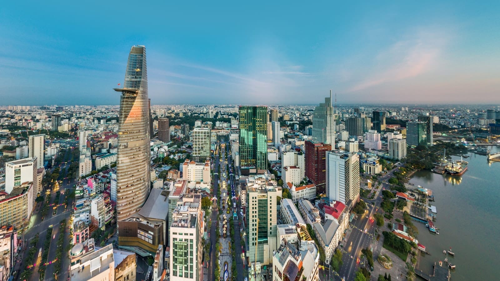 Vista aérea panorámica del horizonte de Ciudad Ho Chi Minh con la Torre Bitexco, rascacielos modernos, el río Saigón y calles bulliciosas bajo un cielo azul despejado.