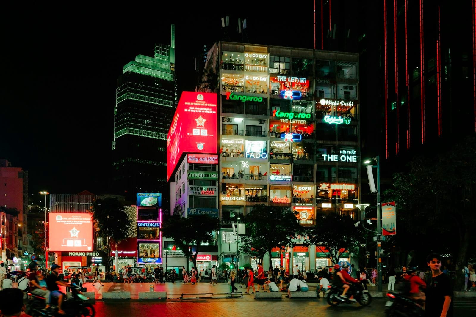 Un edificio en Ho Chi Minh City con varios bares y salones iluminados visibles a través de las ventanas, con personas y scooters en primer plano de noche.