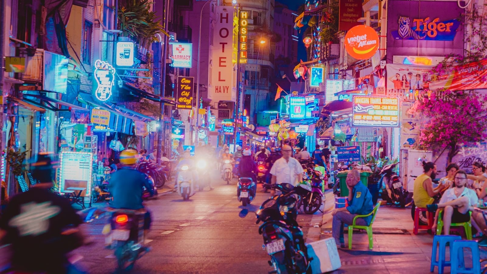 Animada escena nocturna de Ho Chi Minh City con bares iluminados con neón, motocicletas y personas socializando en la calle en el Distrito 1.