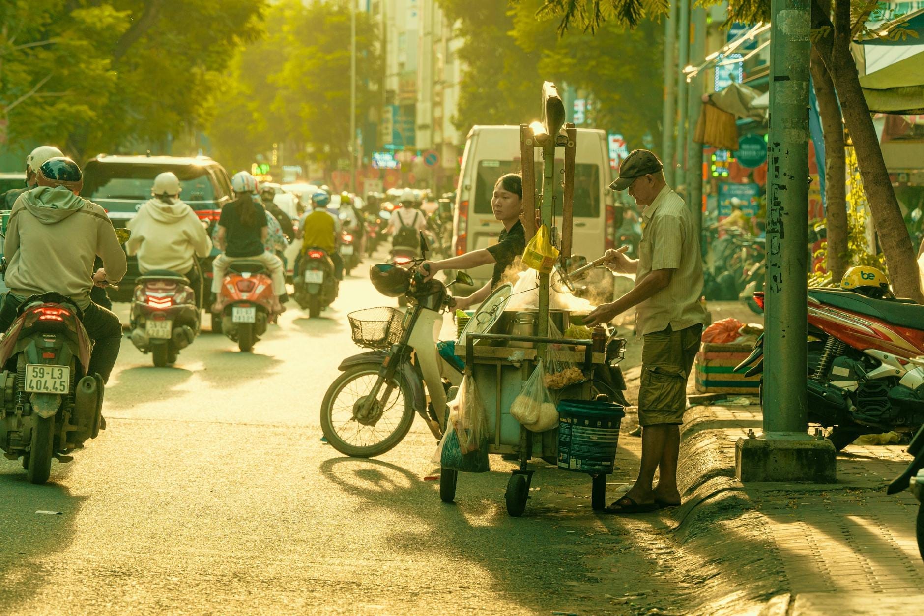 Un vendedor ambulante de comida sirve platillos desde un carrito en una concurrida calle de Ho Chi Minh City, con la luz del sol iluminando la animada escena.