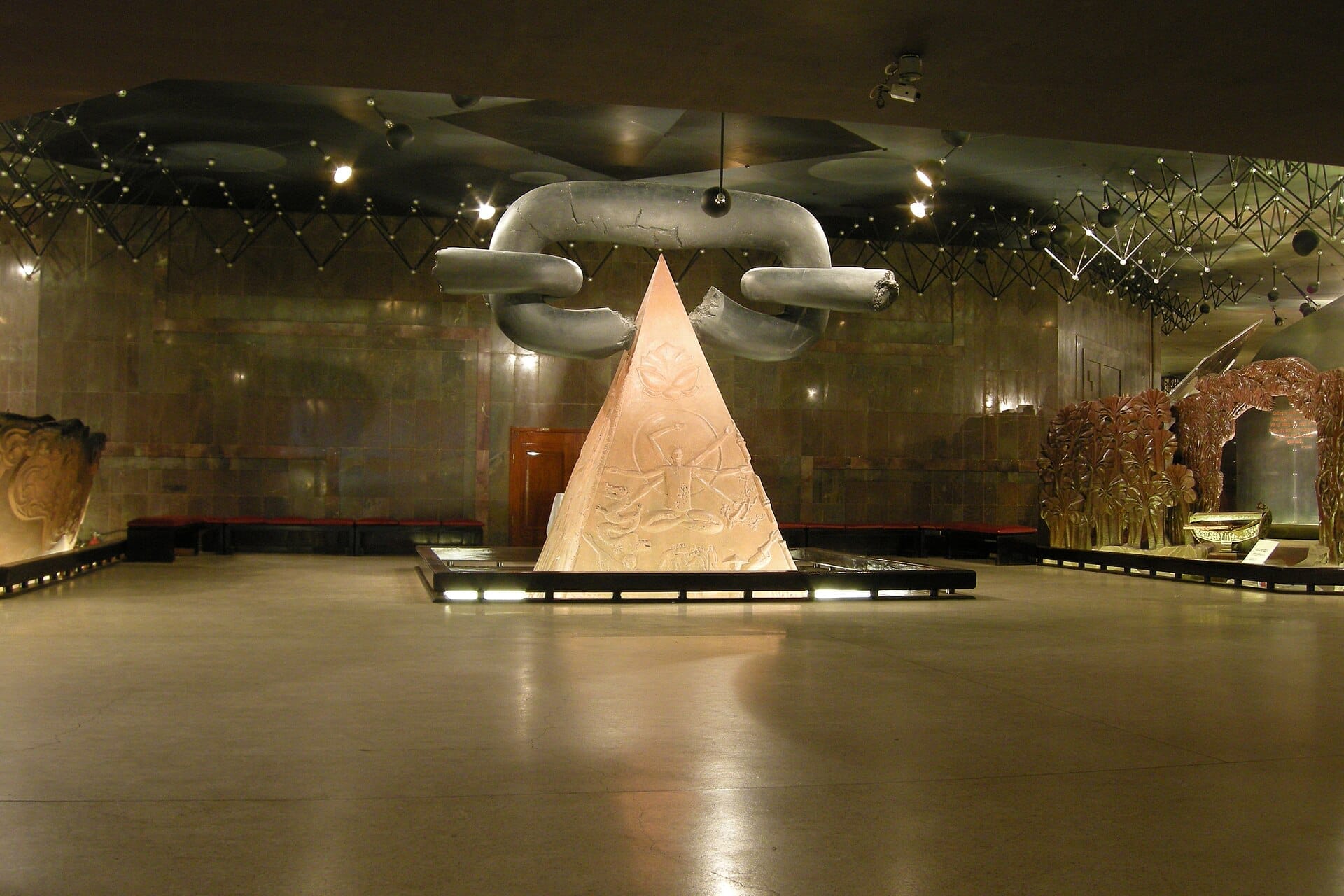 Central hall of the Ho Chi Minh Museum featuring a large pyramidal sculpture and oversized metal chain links under dramatic lighting.