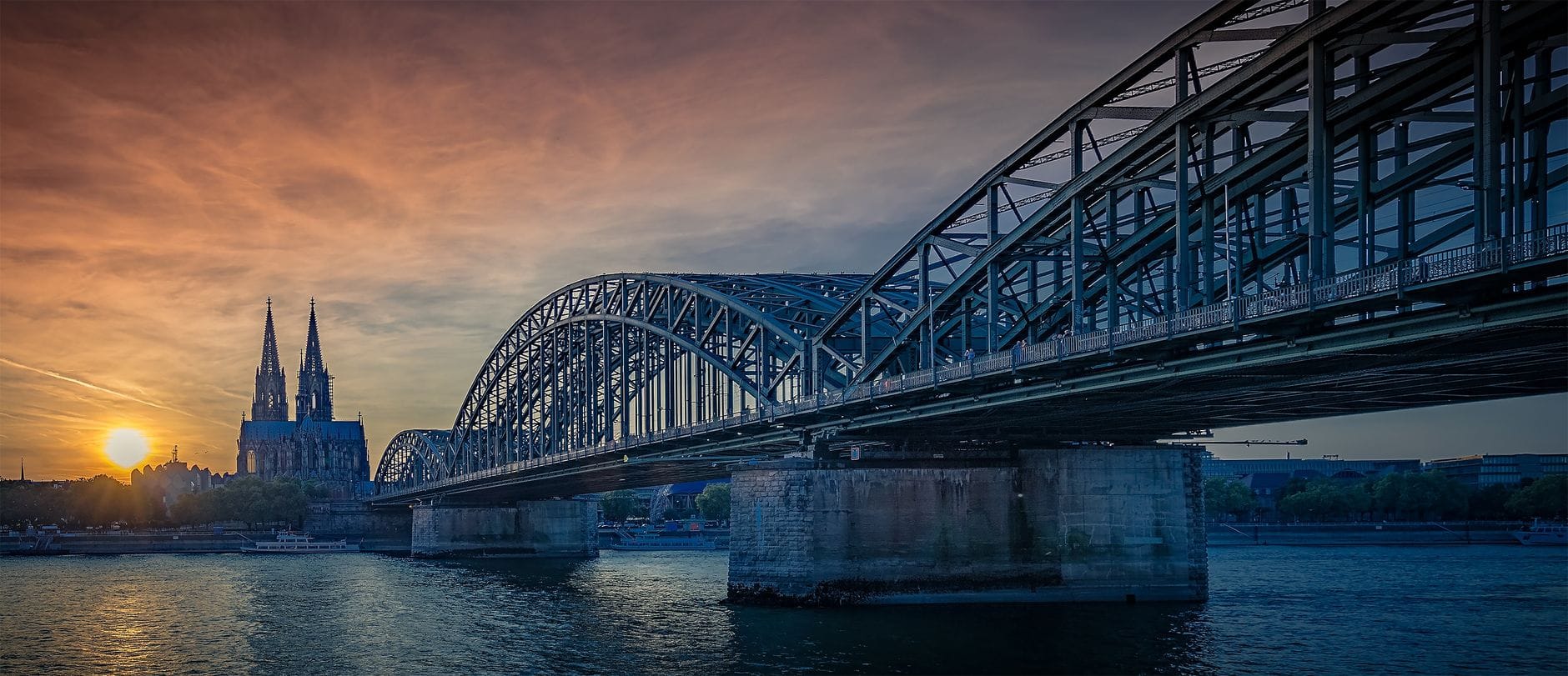 สะพานโฮเฮนโซลเลิร์นข้ามแม่น้ำไรน์ในโคโลญจน์ยามพระอาทิตย์ตก มองเห็นมหาวิหารโคโลญจน์และท้องฟ้าสวยงามตระการตาเป็นฉากหลัง