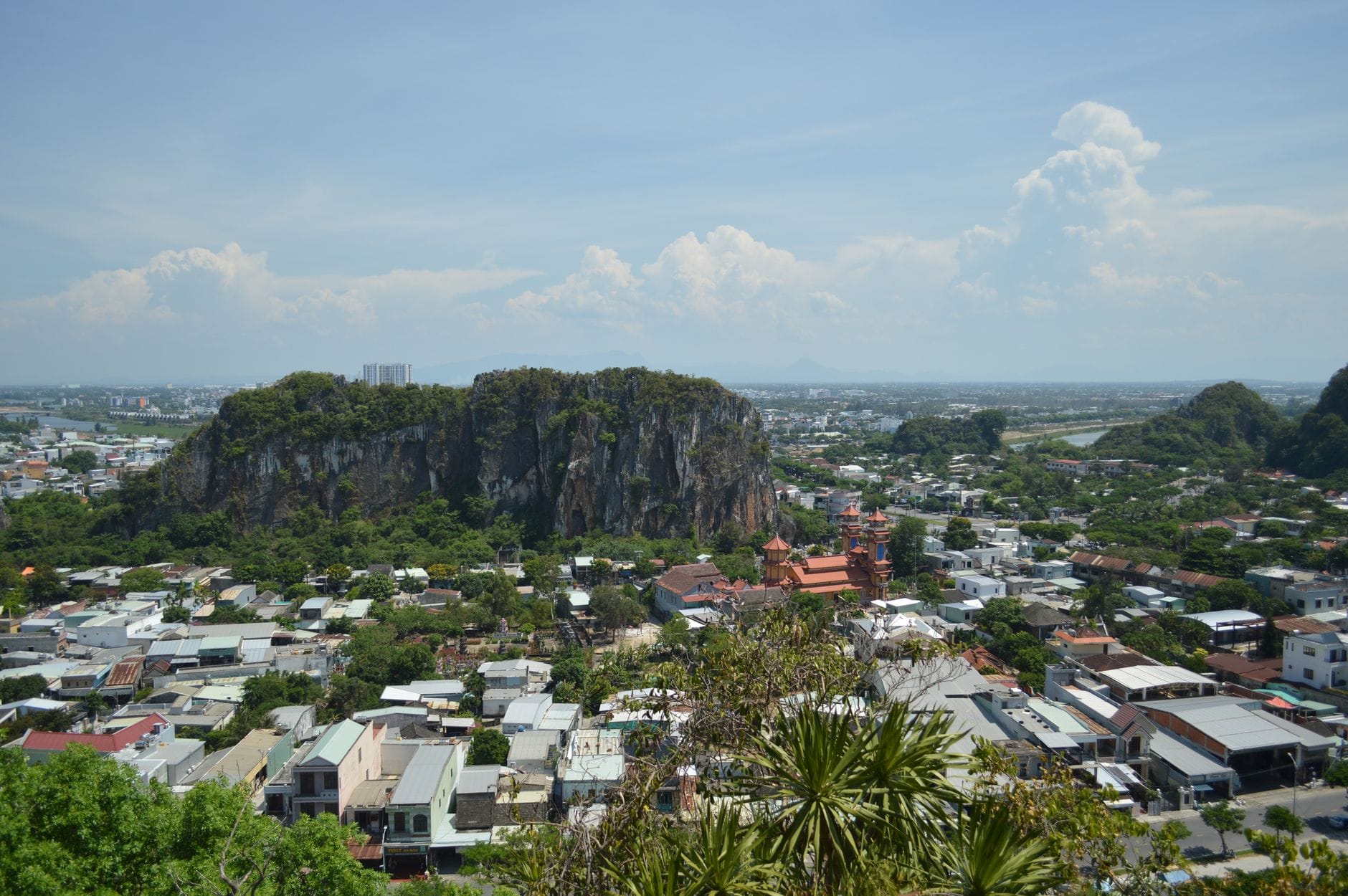 วิวทิวทัศน์ของ Marble Mountains ที่ตั้งตระหง่านเหนือชานเมือง พร้อมบ้านเรือนและพื้นที่สีเขียวกระจัดกระจายในเบื้องหน้าภายใต้ท้องฟ้าสีฟ้า
