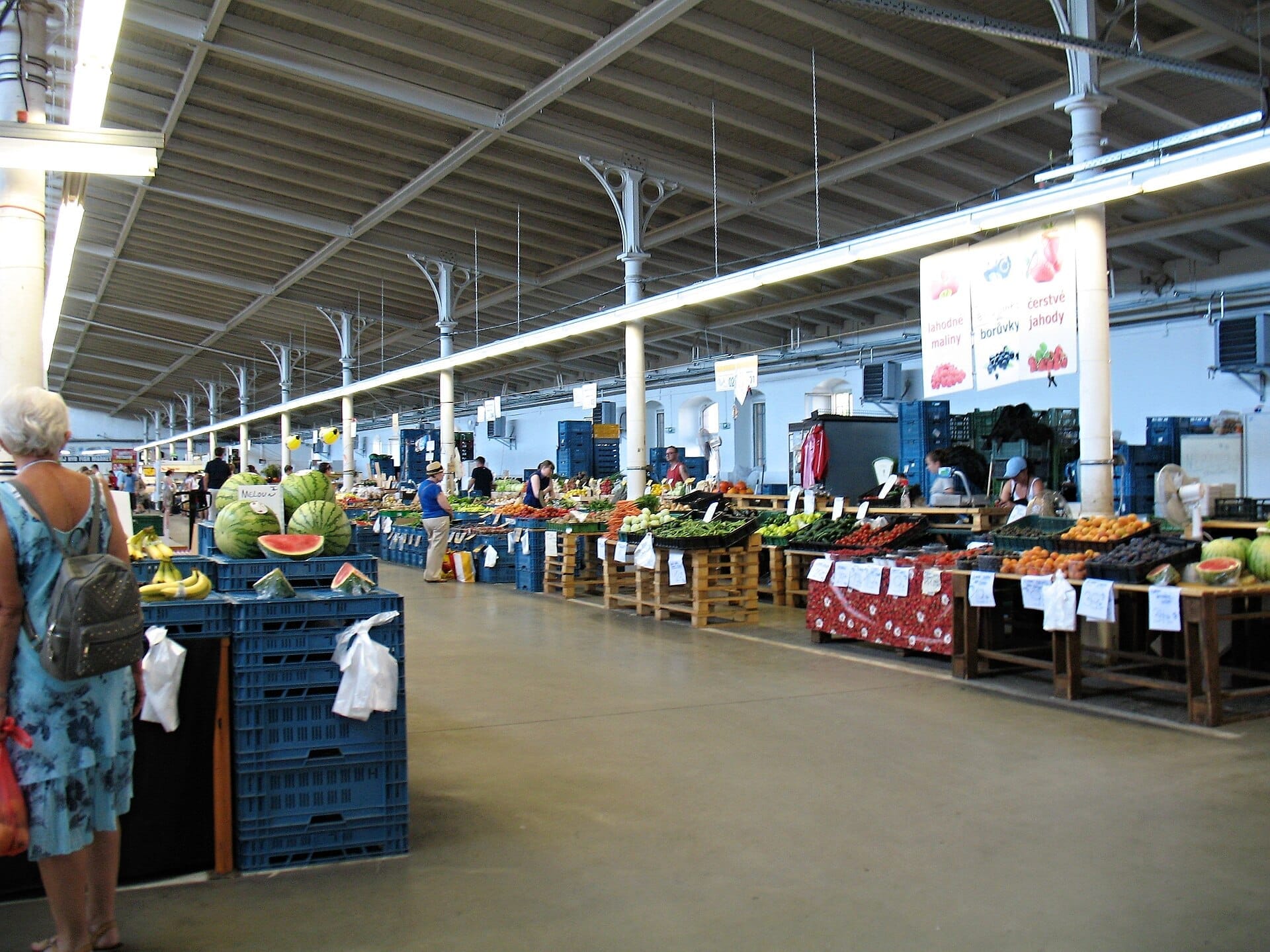 Innenansicht der Markthallen Holešovice in Prag, mit Ständen für frische Produkte, Marktständen und Besuchern unter einer hohen Industriedecke.