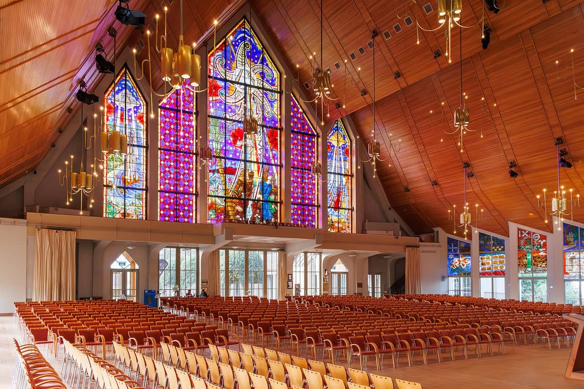Innenraum der Holy Trinity Cathedral in Auckland mit moderner Holzdecke, markanten Buntglasfenstern und Stuhlreihen im Kirchenschiff.