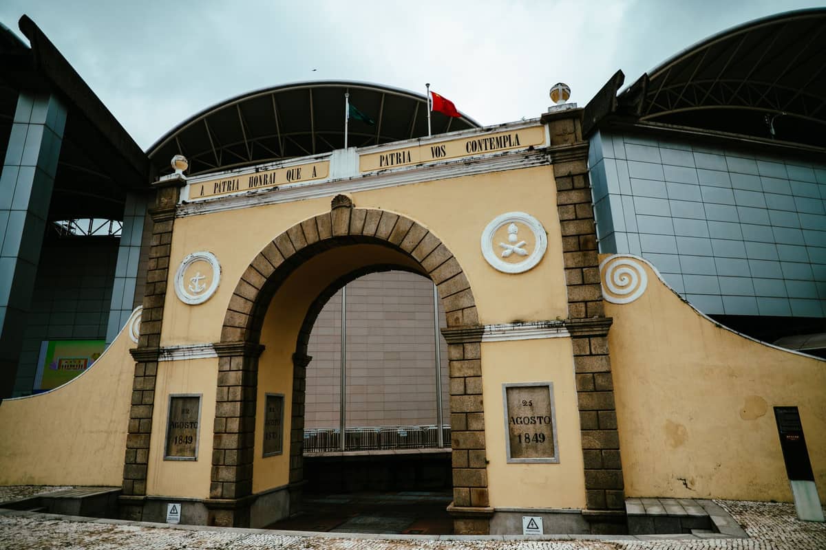 Historisches Bogentor an der Grenze neben einem modernen Gebäude in Macau, das auf Grenzübergang und Terminal-Logistik hinweist.