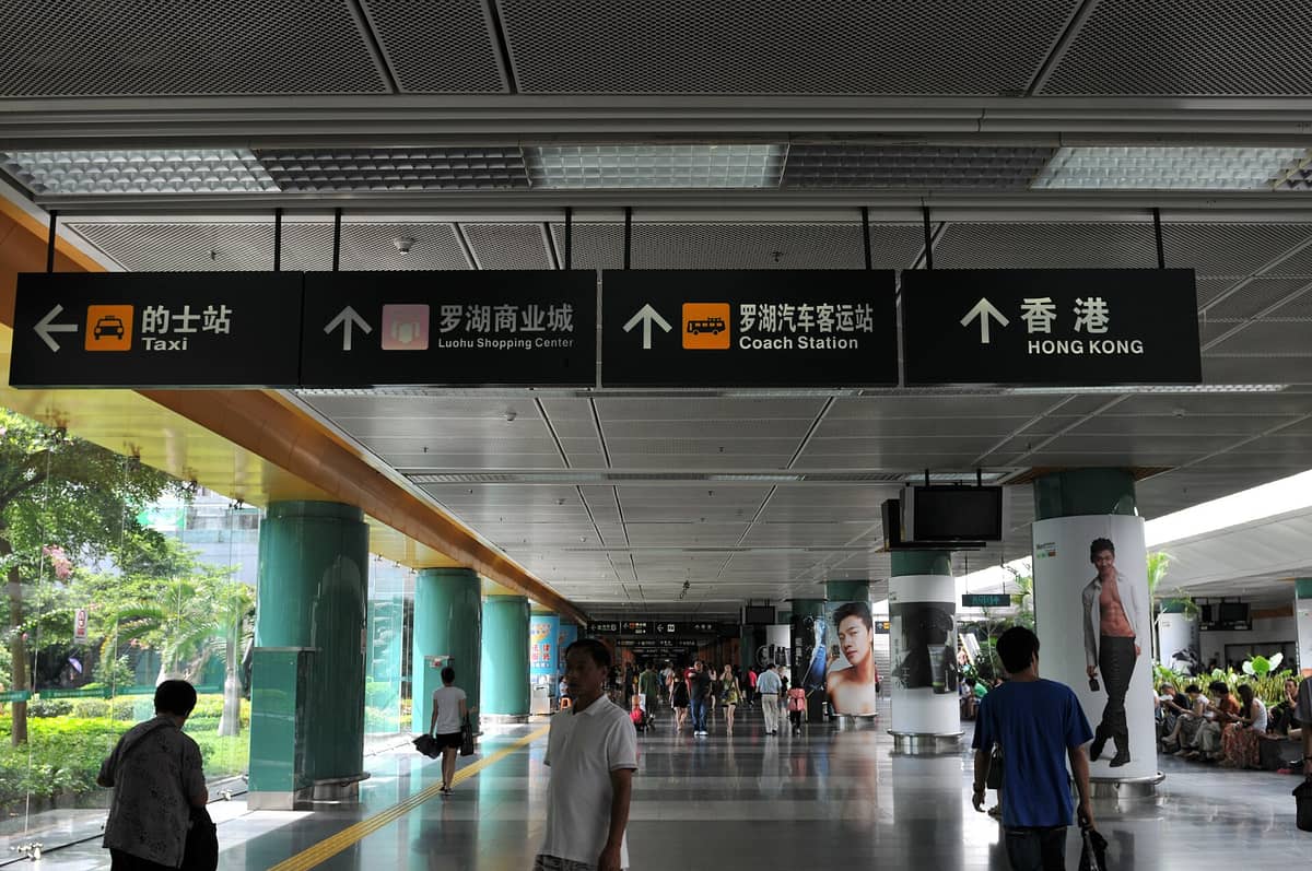 Corredor interno na travessia de fronteira de Luohu em Shenzhen, com sinais claros apontando para Hong Kong e outros destinos.
