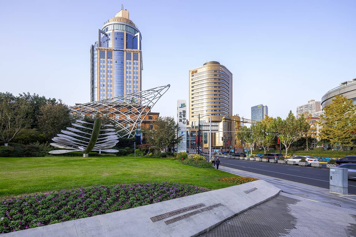 Skulptur und Grünflächen am North Bund in Hongkou, Shanghai, mit markanten modernen Türmen und einer Stadtstraße unter klarem Morgenhimmel.