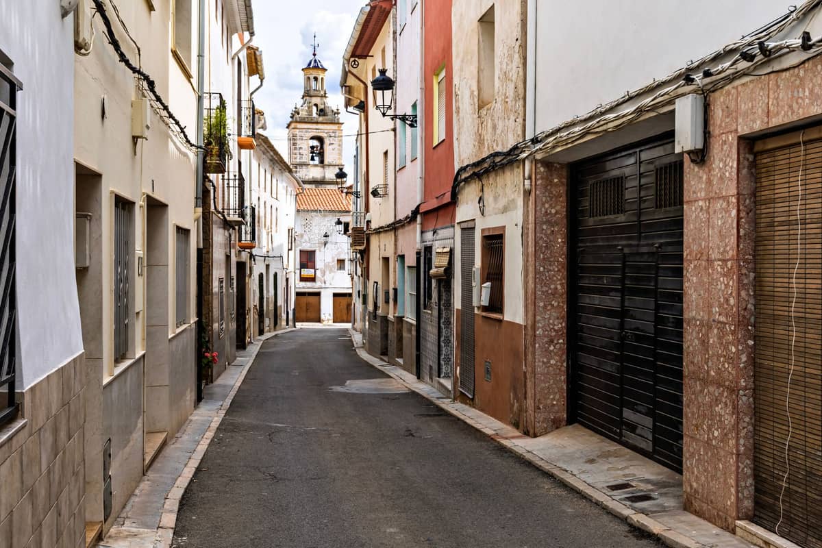 Calle estrecha en Alboraya con casas tradicionales y torre de iglesia al fondo, típica del ambiente del pueblo cerca de Valencia.