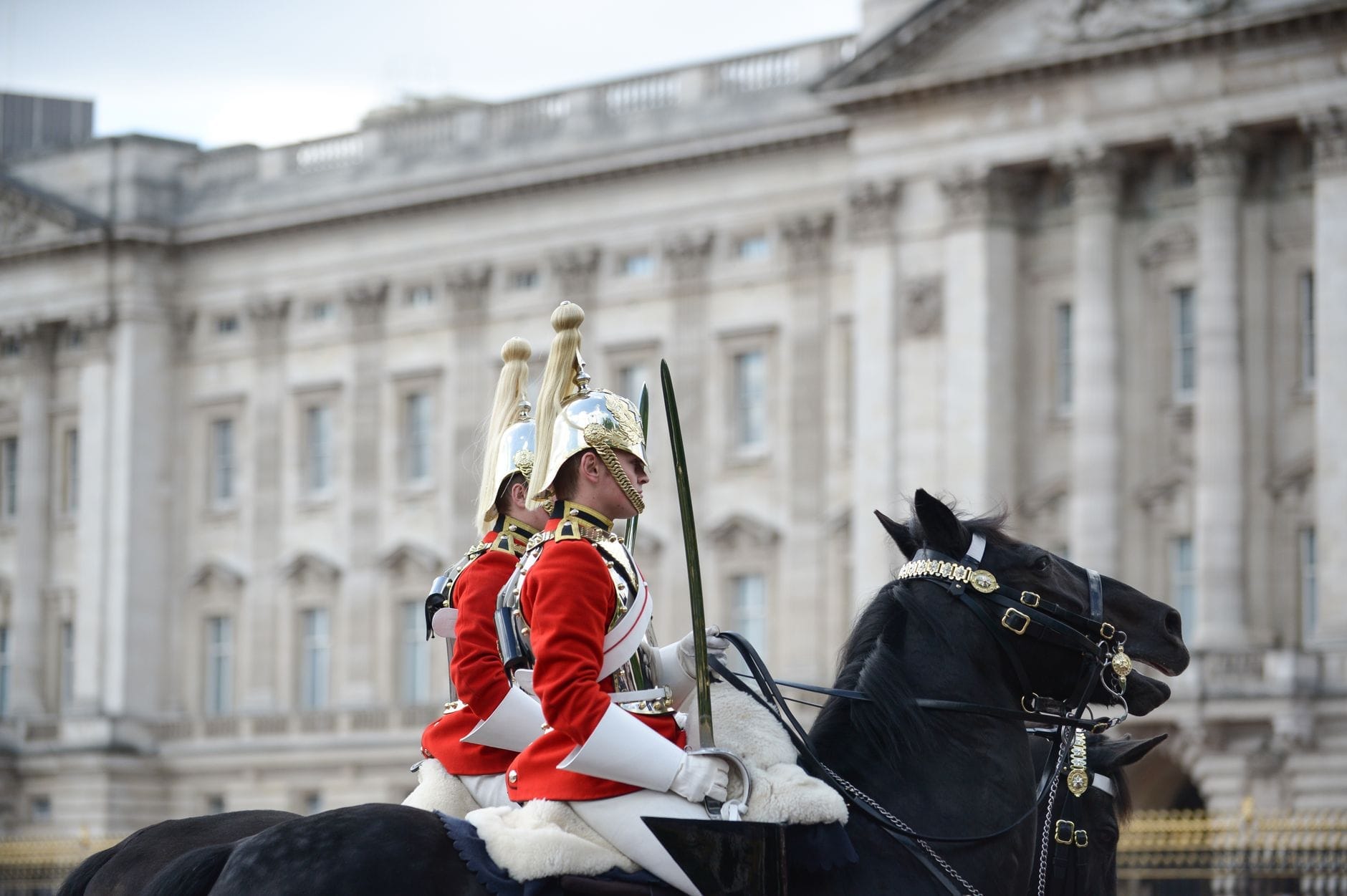 Due soldati a cavallo in uniformi cerimoniali rosse ed elmi argentati sfilano davanti alla grande facciata in pietra di Horse Guards Parade a Londra.