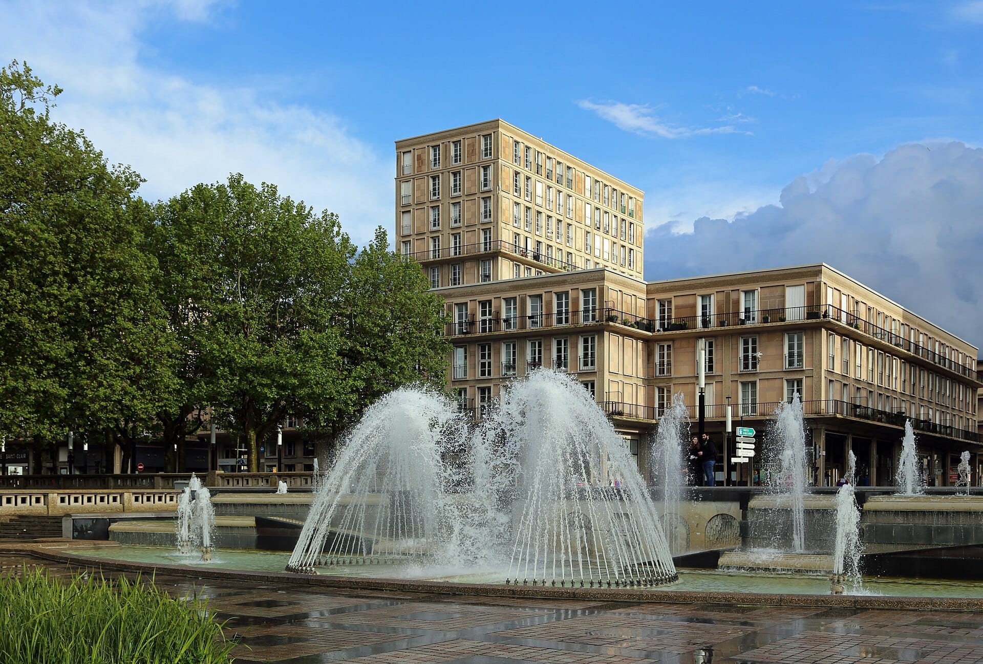 L'Hôtel de Ville du Havre si erge dietro una vivace fontana e alberi verdi sotto un cielo azzurro limpido.