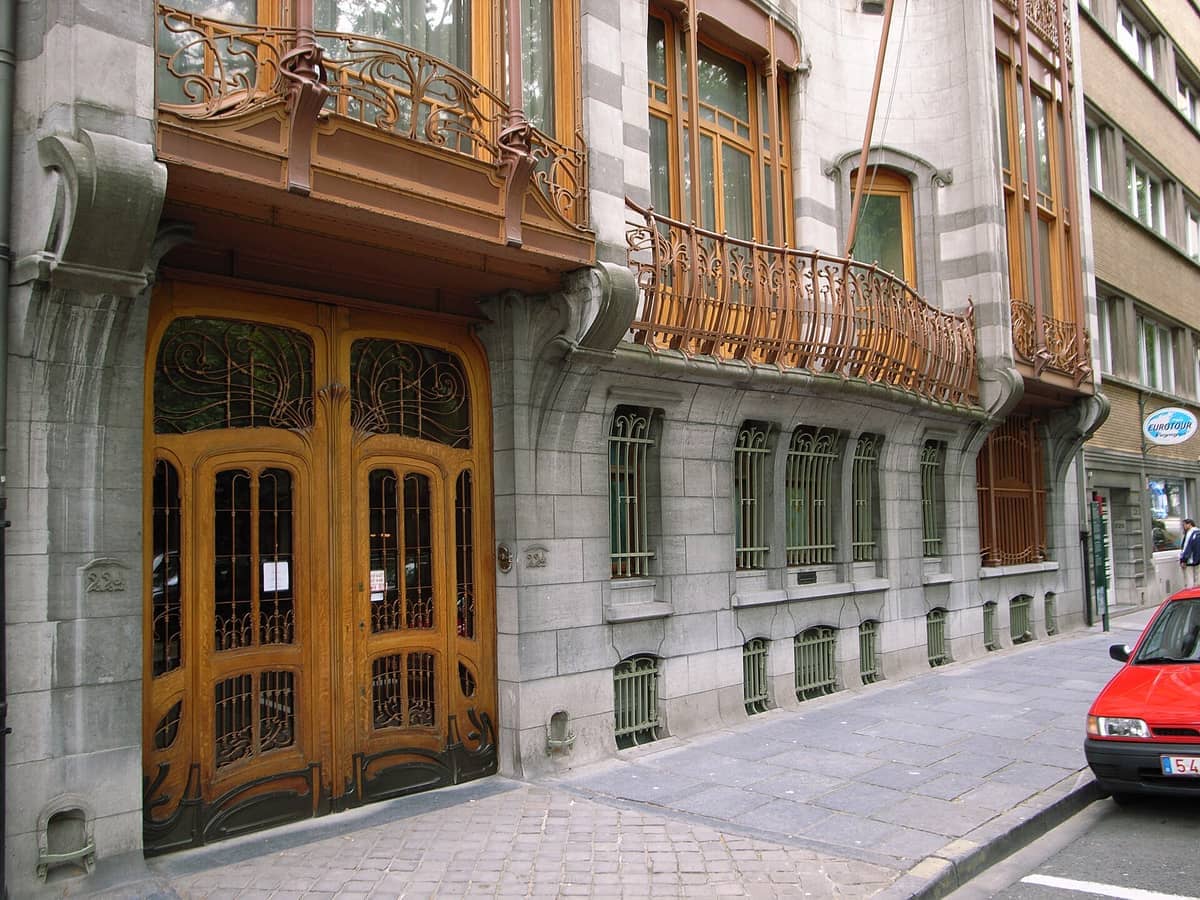 A fachada frontal do Hôtel Solvay em Bruxelas exibe elaboradas ferragens Art Nouveau, grandes portas de madeira e uma arquitetura de pedra curvilínea em uma rua da cidade.