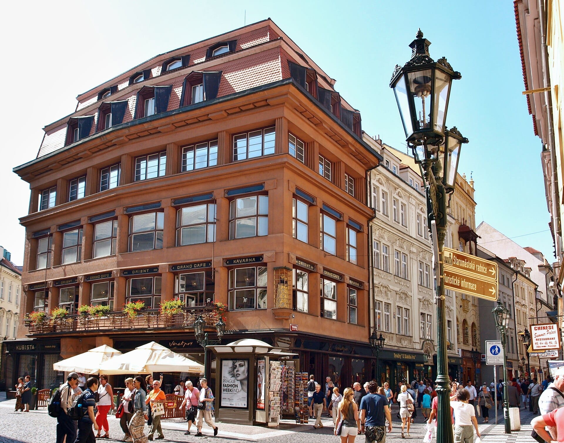 Haus zur Schwarzen Muttergottes in Prag, markante kubistische Architektur mit großen Fenstern, Straßencafé und Touristen bei sonnigem Wetter.
