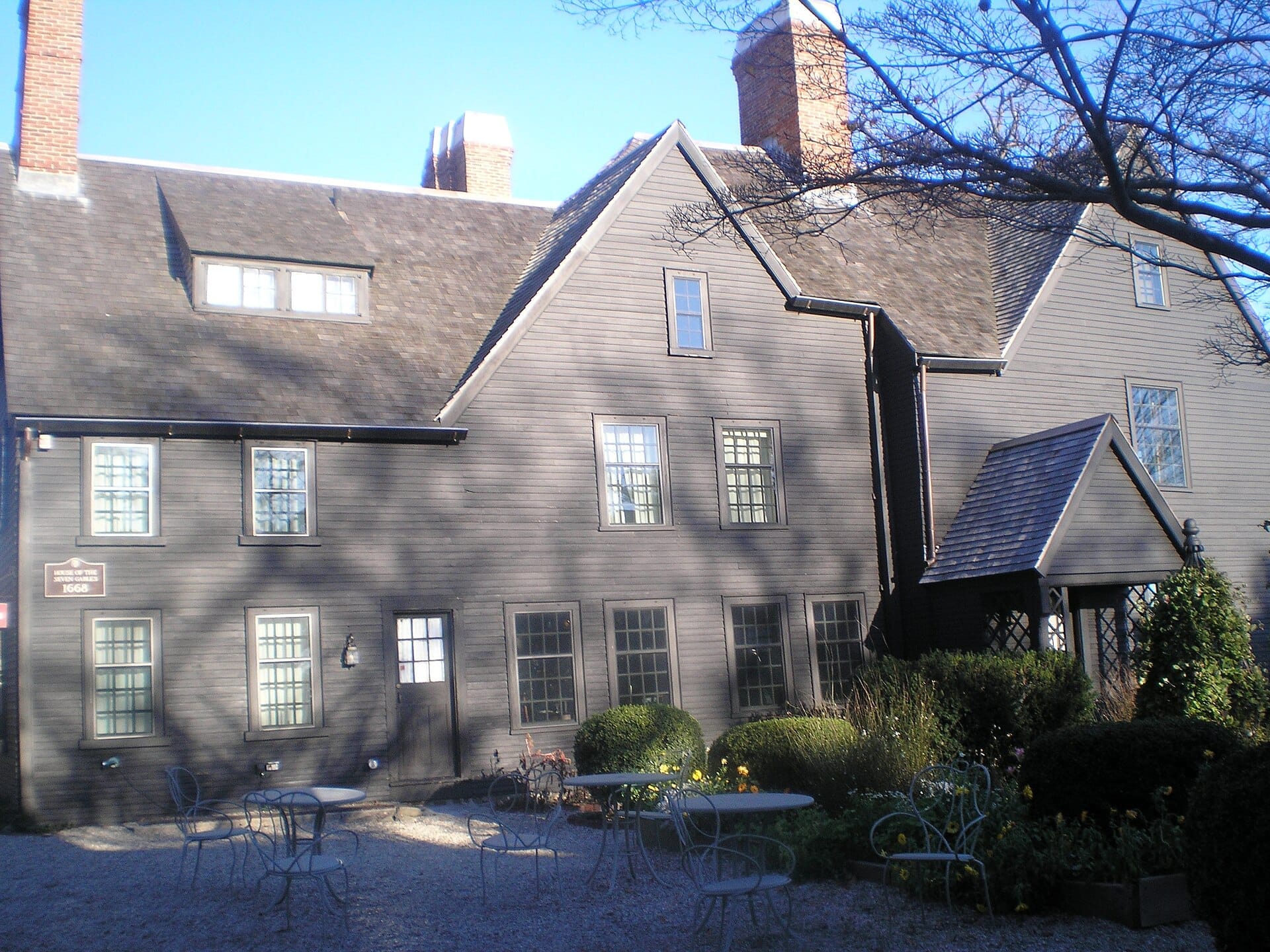 La House of the Seven Gables a Salem, uno storico maniero in legno scuro con più frontoni, camini in mattoni e un'area salotto nel giardino esterno.