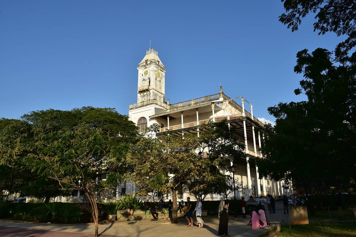 Vista panoramica della Casa delle Meraviglie (Beit al-Ajaib) a Stone Town, Zanzibar, con la torre dell'orologio, le alte colonne bianche e le verande aperte; in primo piano alcuni visitatori.