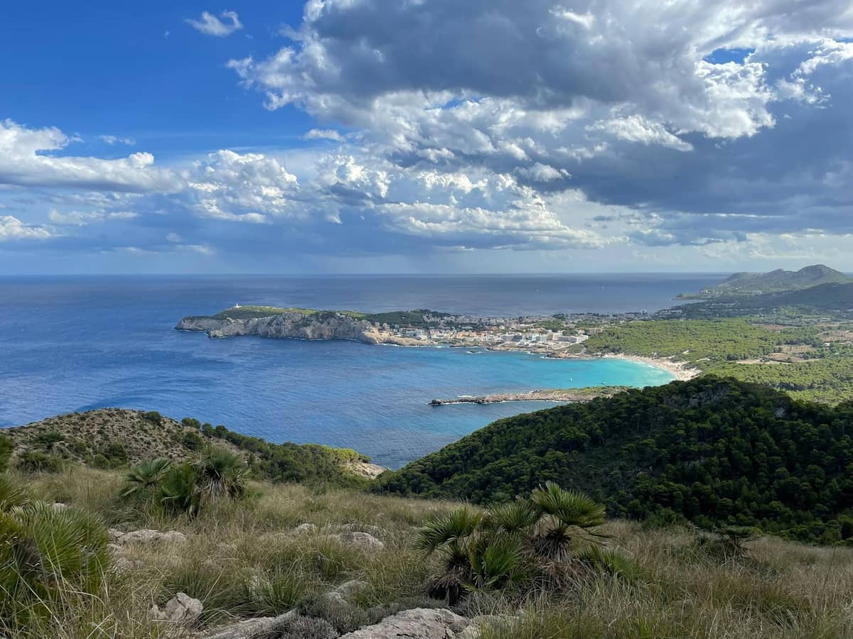 Yeşil tepeler, bir plaj ve farklı hava koşullarına işaret eden değişken bulutlarla Mallorca kıyı şeridinin geniş görünümü.