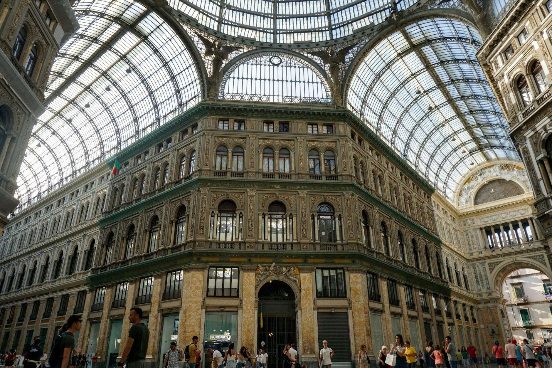 Des personnes se promenant et se rassemblant sous le grand dôme en verre de la Galleria Umberto I à Naples, avec une architecture historique ornée.