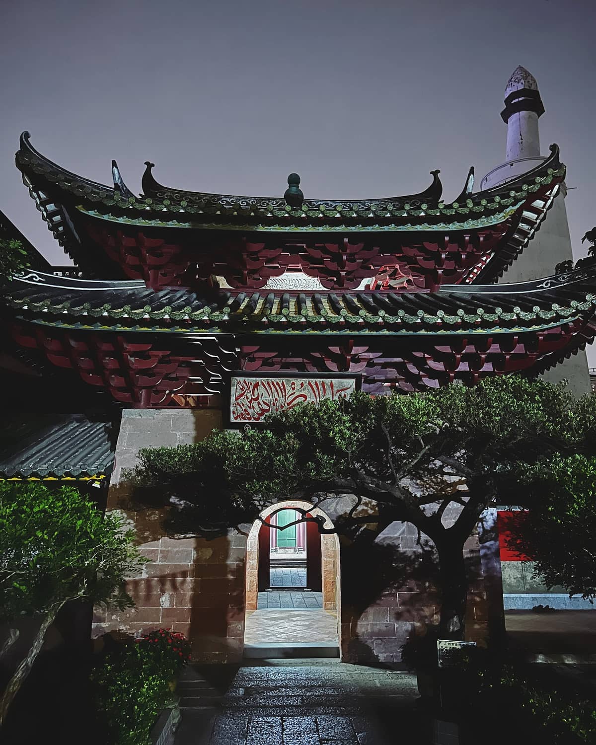 Night view of Huaisheng Mosque’s entrance with traditional curved roof, illuminated pathway, and circular white minaret in Guangzhou, China.