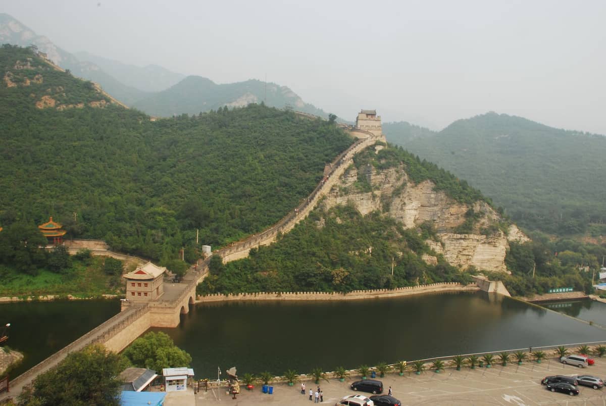 Die Chinesische Mauer bei Huanghuacheng führt direkt in einen Stausee, umgeben von grünen Hügeln und Wasser am Fuß der Mauer.
