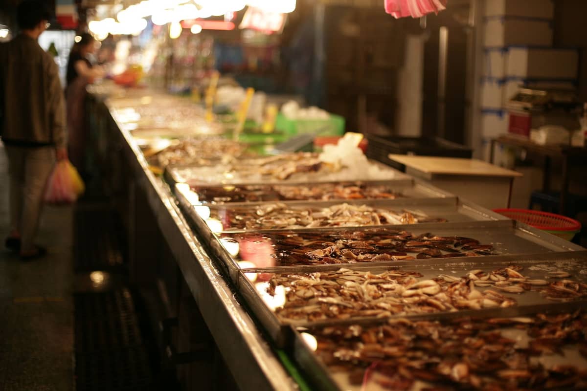 Rows of seafood tanks filled with live crabs and shellfish inside an indoor seafood market, with bright lighting and people shopping in the background.