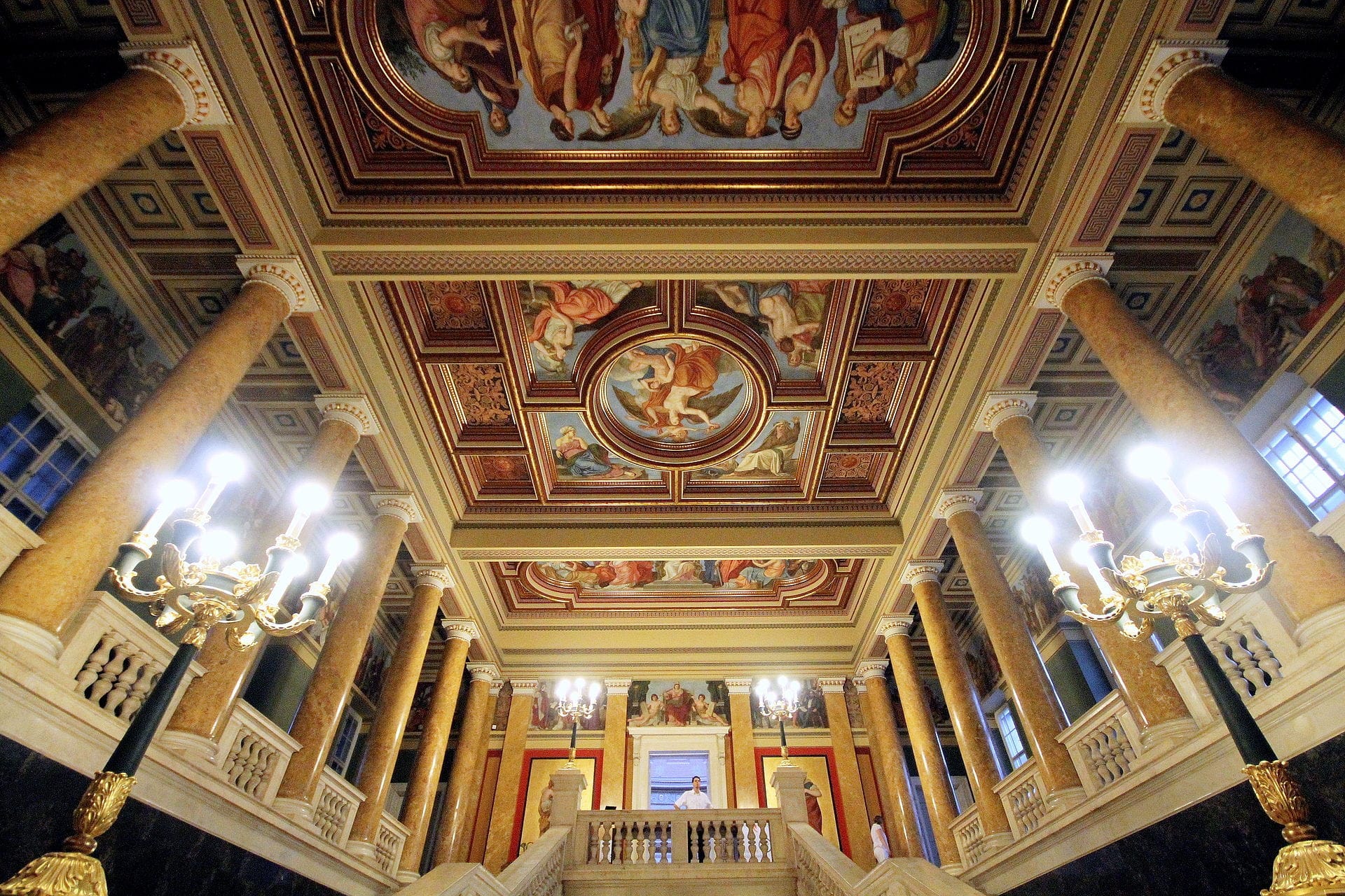 Große Treppenhalle des Ungarischen Nationalmuseums mit verzierten Kronleuchtern, Marmorsäulen und einer detailreichen neoklassizistischen Deckenmalerei.