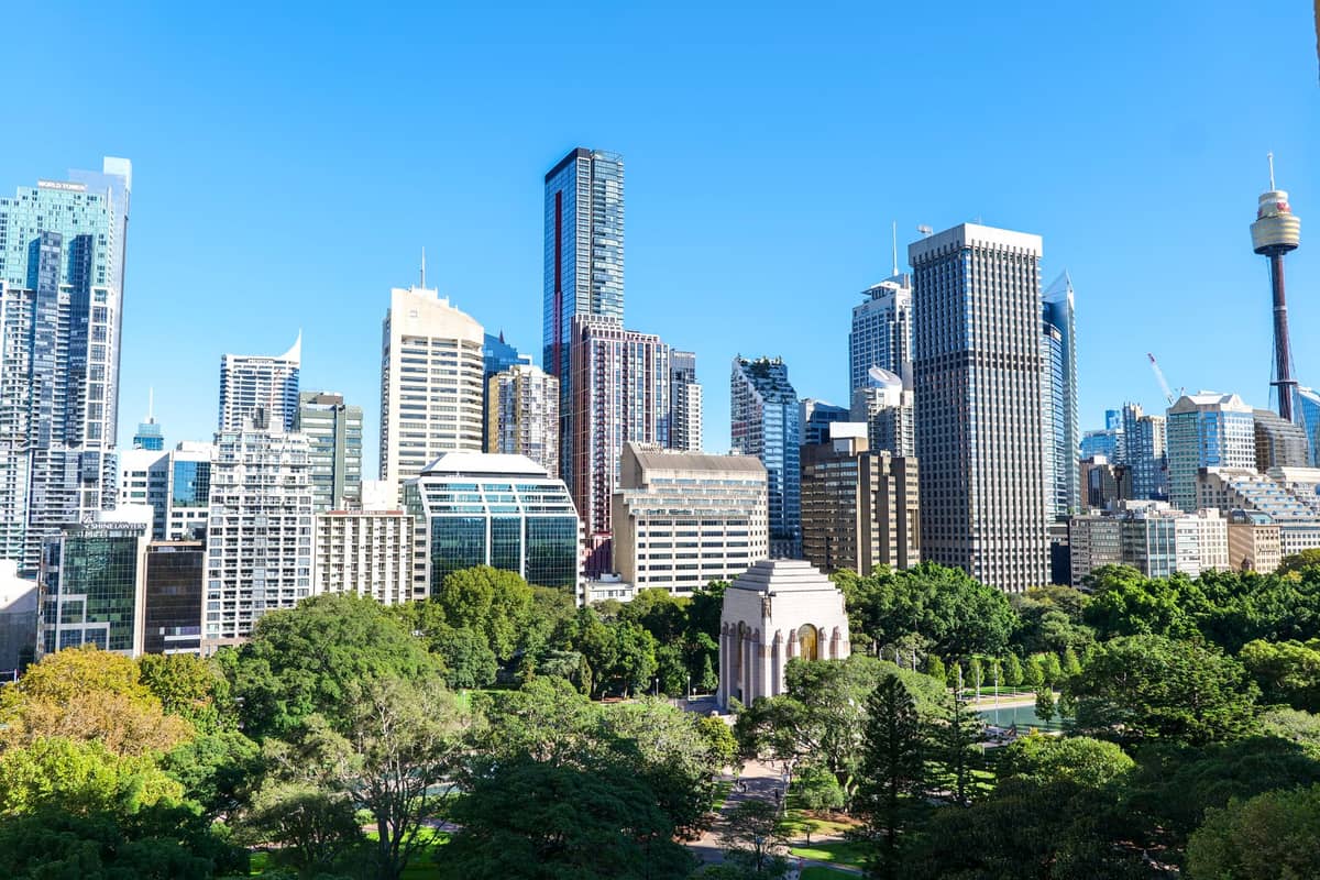 Vista aerea di Hyde Park a Sydney con alberi rigogliosi, l'ANZAC War Memorial e i grattacieli della città circostante in una giornata limpida e luminosa.