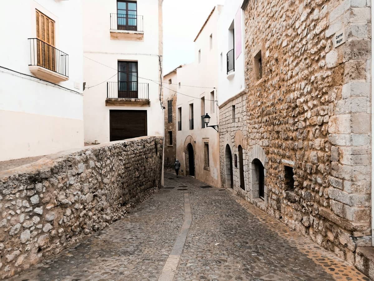 Cobbled street winding between whitewashed and stone buildings in Dalt Vila, Ibiza's old town, with no crowds and soft natural light.