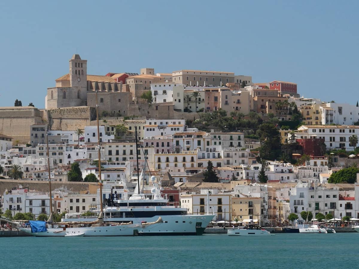 View of Dalt Vila in Ibiza showing the fortified old town atop a hill, white hillside buildings, and yachts in the harbor.