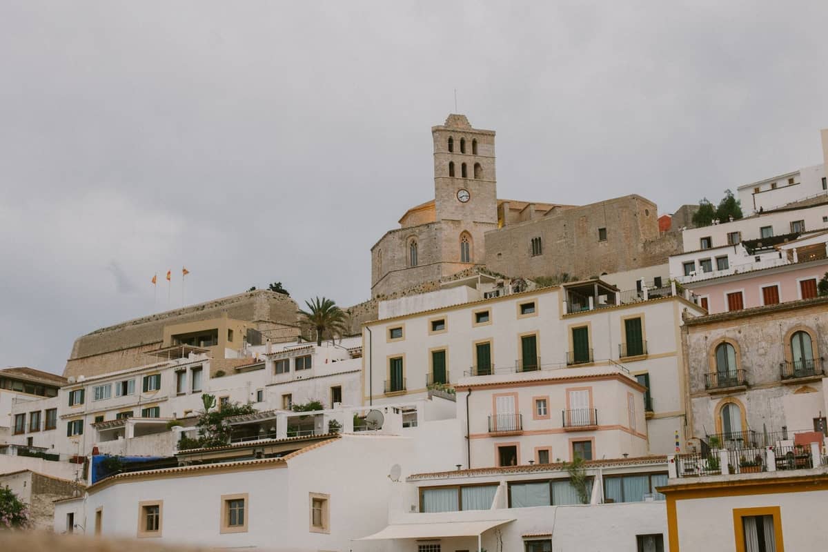 View of the Ibiza Cathedral rising above whitewashed homes inside Dalt Vila’s old town walls, under cloudy skies