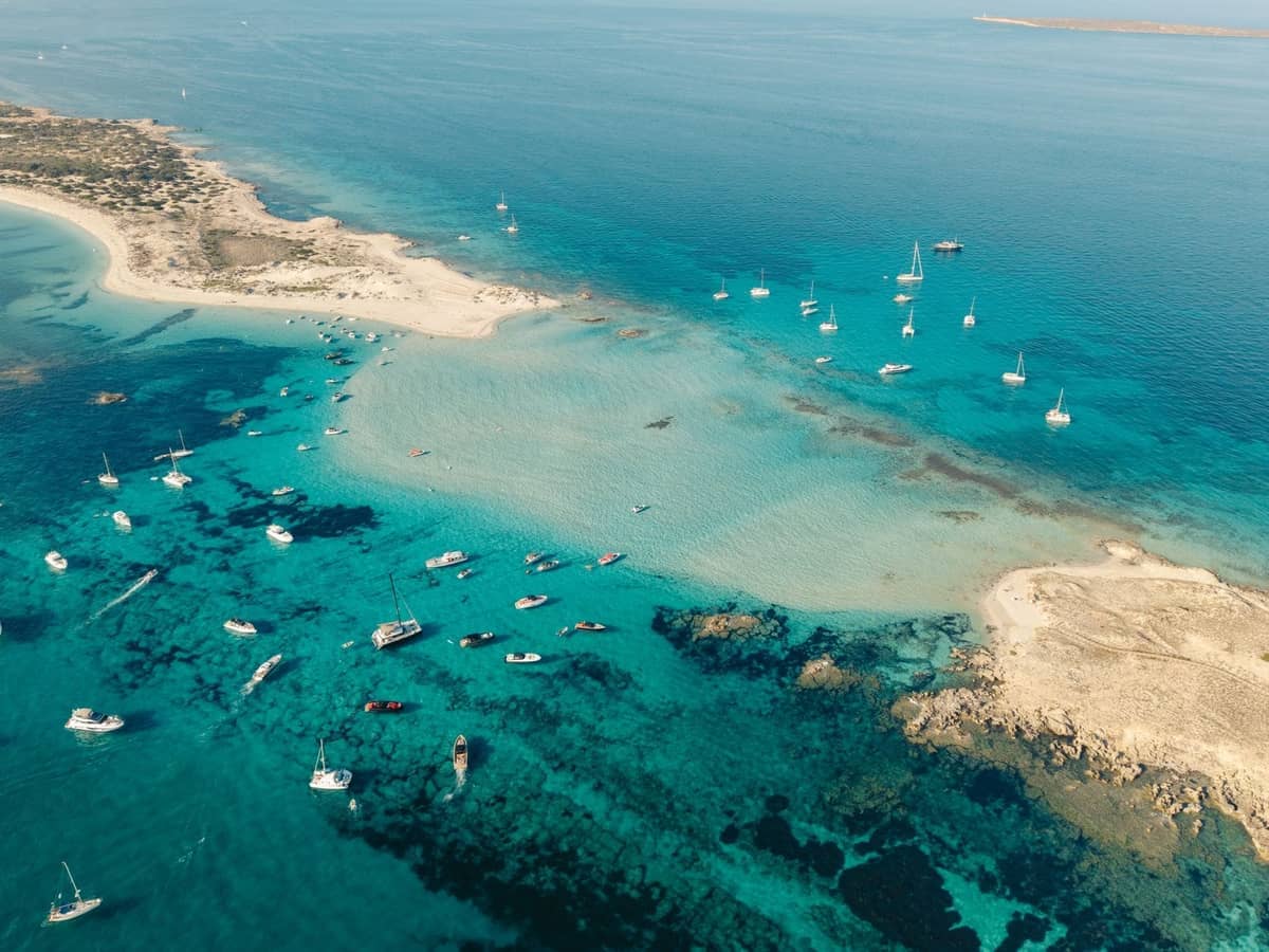 Aerial view of turquoise sea, sandy islets, and anchored boats between Ibiza and Formentera, capturing the essence of island escapes.