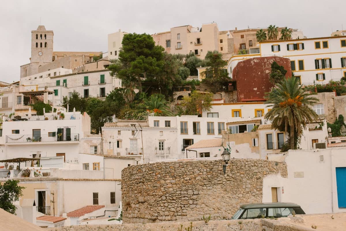 Cluster of whitewashed village houses and a stone structure with a church above, nestled on a hill in historic Ibiza.