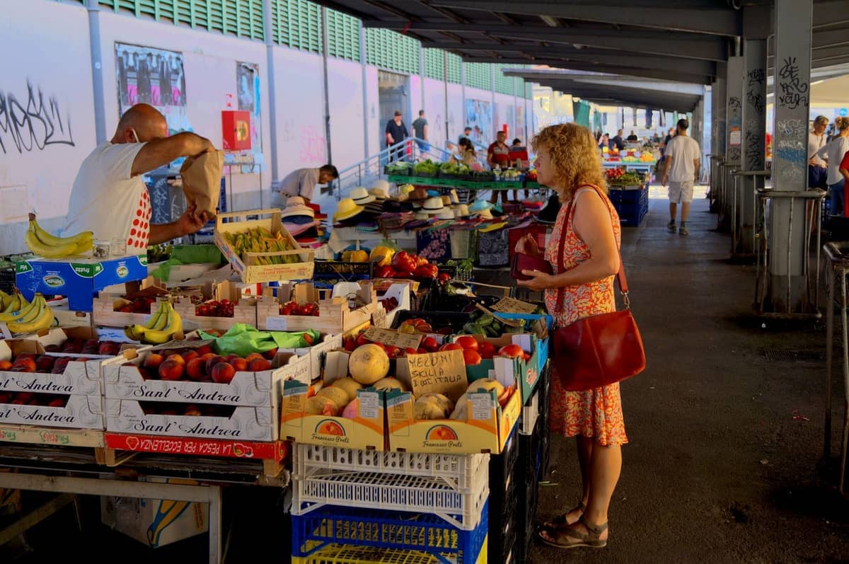 Outdoor village market with fruit and vegetable stalls, local people shopping, and a relaxed, authentic atmosphere.