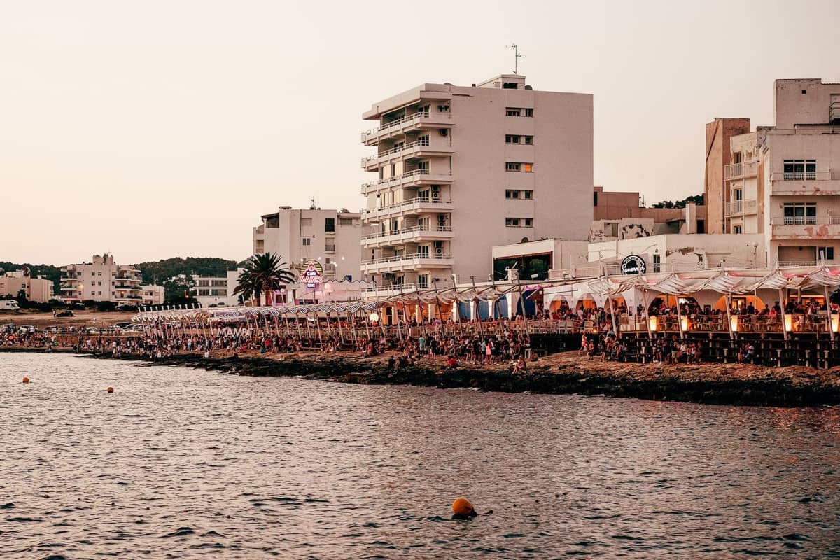 Seafront market stalls along the water’s edge in Ibiza with apartment buildings in the background at sunset.