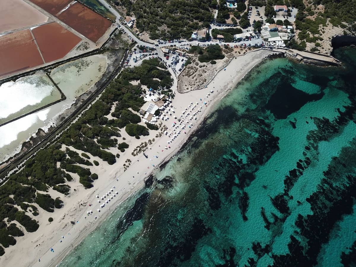 Aerial view of Ses Salines beach with turquoise water, white sand, salt flats, and natural park landscape in southern Ibiza.