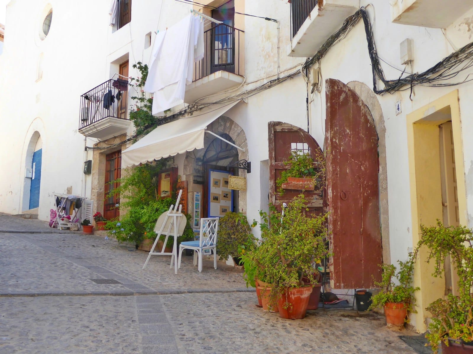 Rua de paralelepípedos na cidade antiga de Dalt Vila em Ibiza com edifícios caiados, vasos de plantas, portas de madeira e roupa pendurada nas varandas.