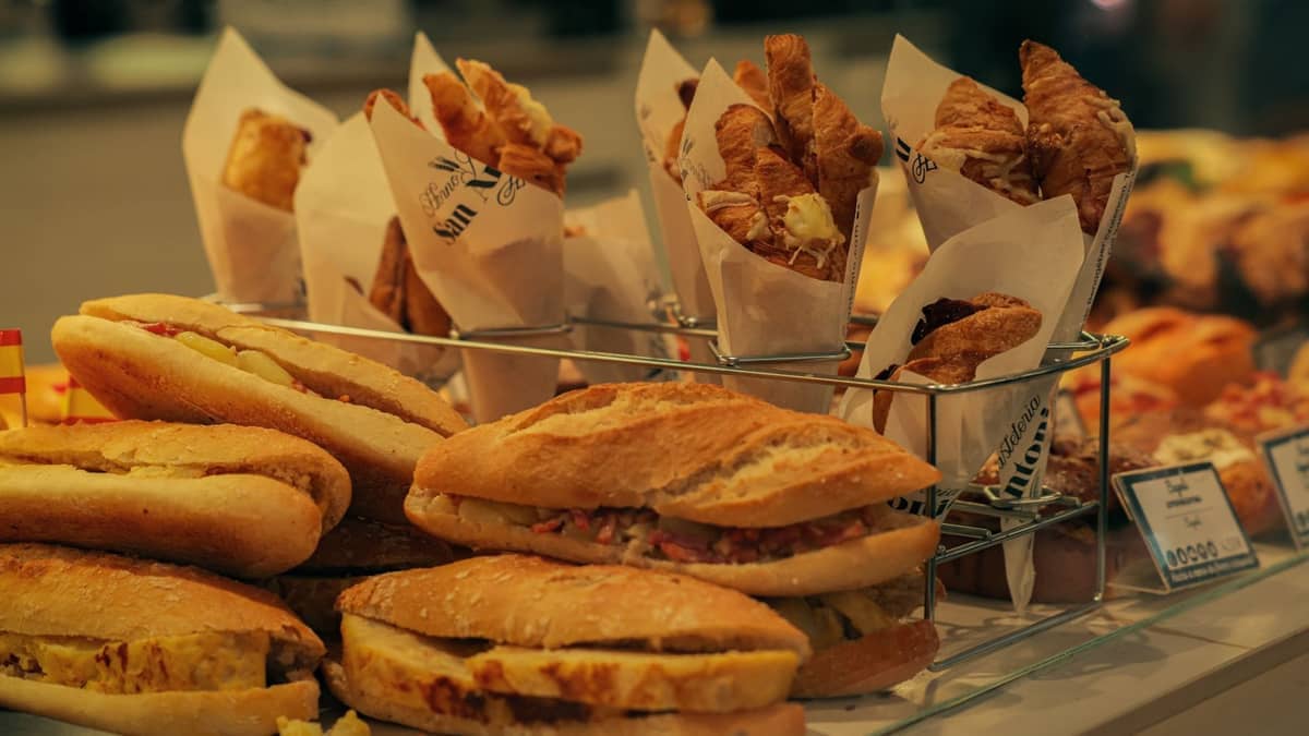 Counter at a bakery with affordable sandwiches and pastries, some in paper cones, suggesting quick, budget-friendly meal options.