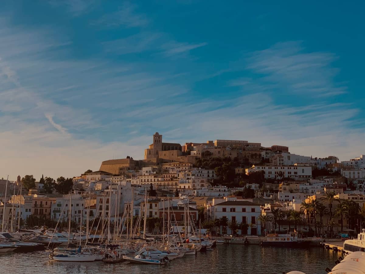 Ibiza Town at sunset with cathedral on the hilltop, harbor, and boats in the golden hour light.