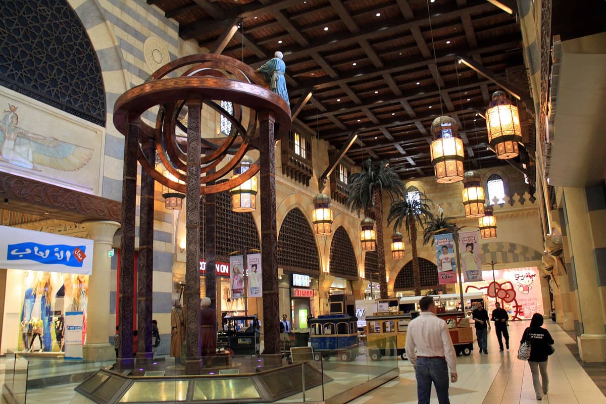 Inneres des Ibn Battuta Malls mit aufwendigem nahöstlichem Architekturdesign, thematischem Dekor, einem großen Astrolabium-Nachbau, Palmen, Laternen, Geschäften und Besuchern, die durch die Haupthalle schlendern.