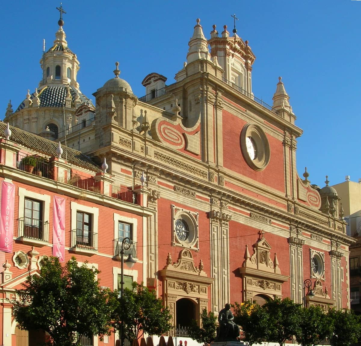 ด้านหน้าของ Iglesia del Divino Salvador ในเมือง Seville พร้อมสถาปัตยกรรมบาโรกที่งดงาม สีแดงและสีครีม และท้องฟ้าสีฟ้าใส