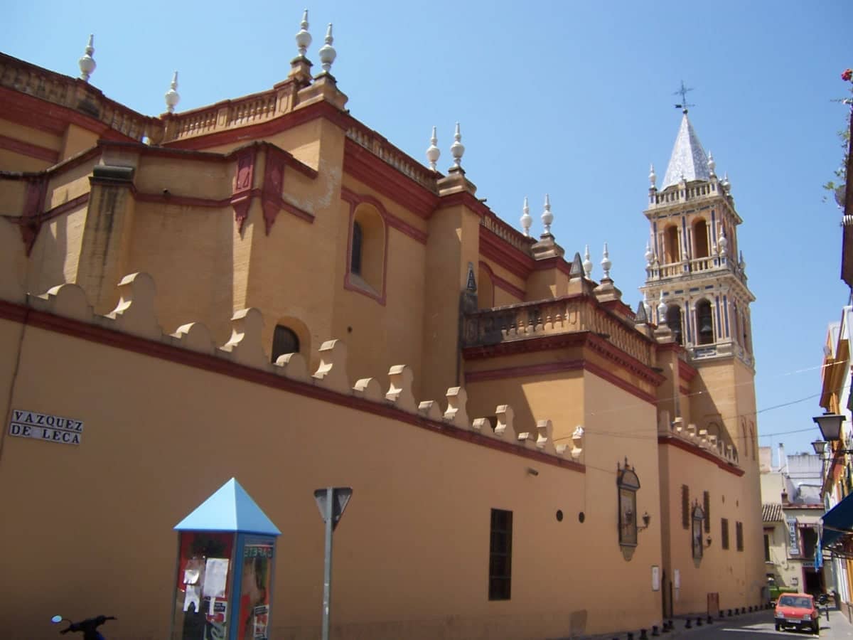 วิวภายนอกของ Iglesia de Santa Ana ในเมืองเซบิยา โดดเด่นด้วยกำแพงสีดินเหลือง ใบเสมาแหลมคม และหอระฆังภายใต้ท้องฟ้าสีฟ้าใส