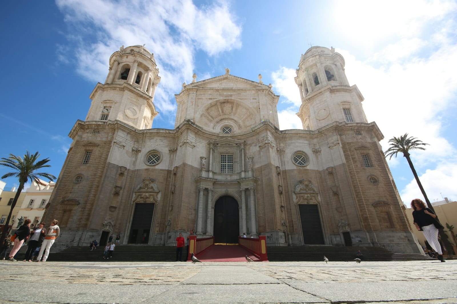 Vista frontale della Iglesia de Santa Cruz a Cádiz, con i suoi due campanili gemelli, la facciata in pietra ornata e le persone riunite nella soleggiata plaza.