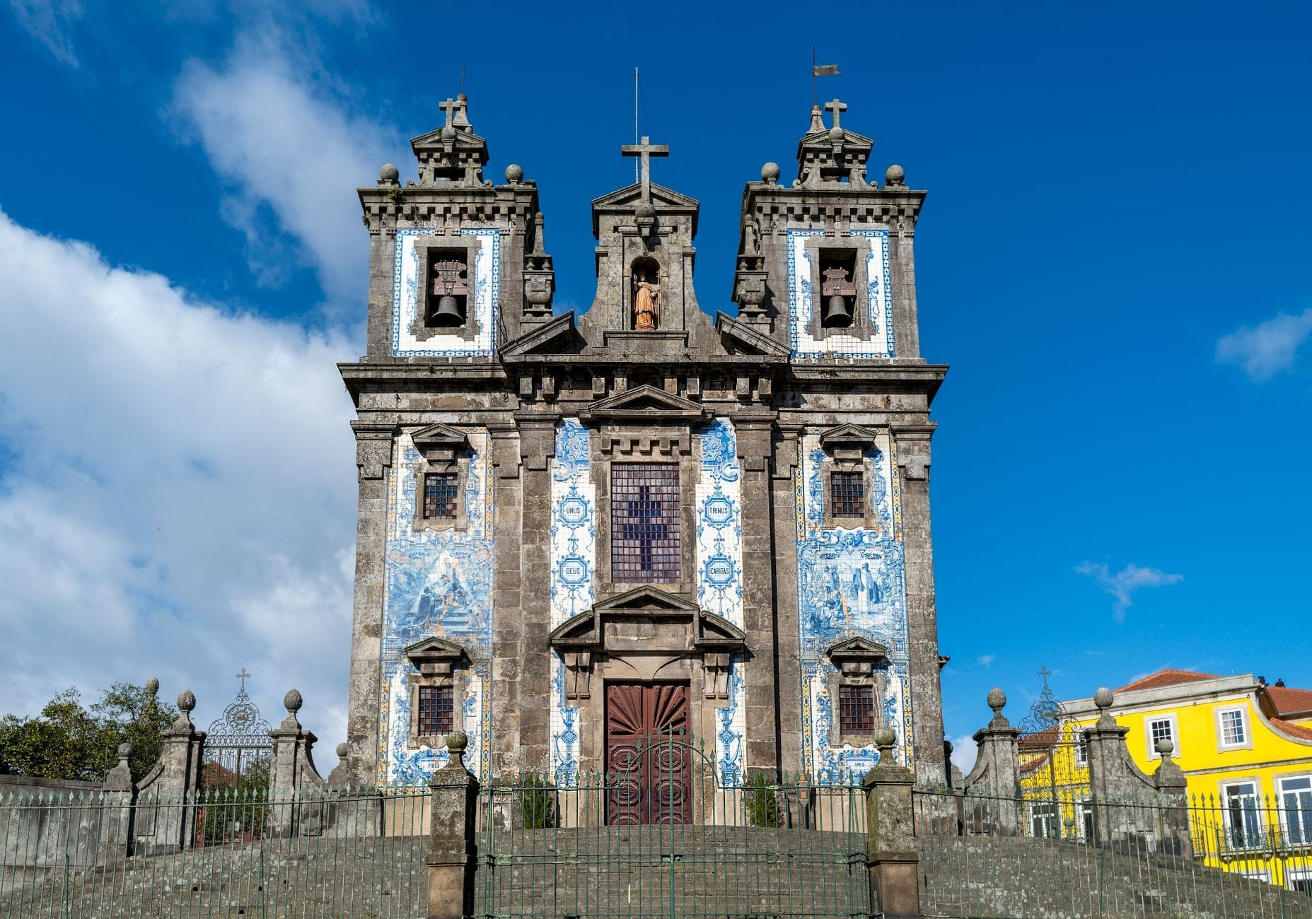 Vista frontale della Igreja de Santo Ildefonso a Porto, con la sua iconica facciata di azulejos blu e bianchi sotto un cielo azzurro intenso e alcuni edifici vivaci nelle vicinanze.