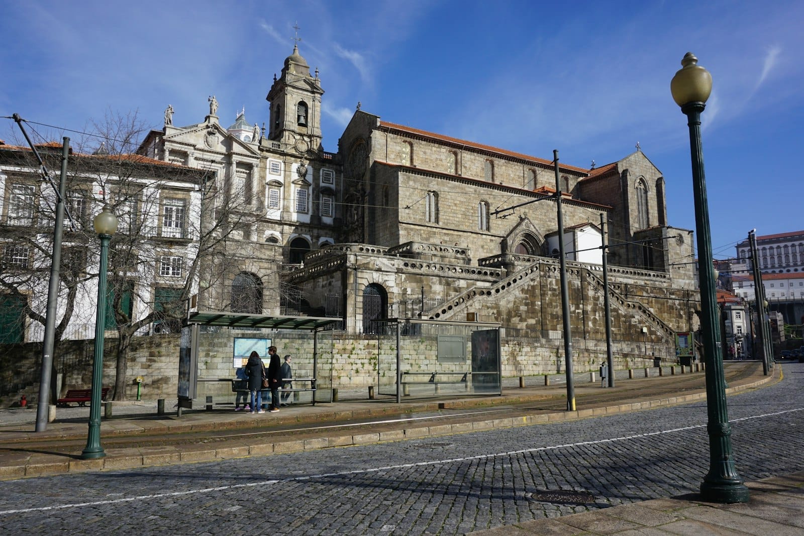 Vista ampia dell'esterno gotico in pietra della Igreja de São Francisco, con le sue scalinate scenografiche e gli edifici adiacenti a Porto, sotto un cielo azzurro e luminoso.